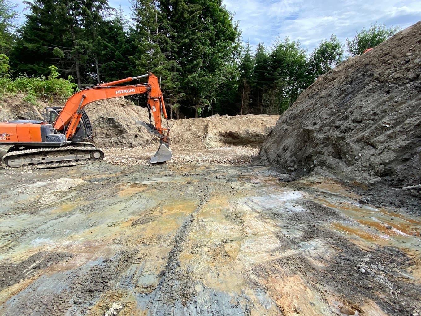 An excavator working in a raw cut with exposed layers of bedrock strata