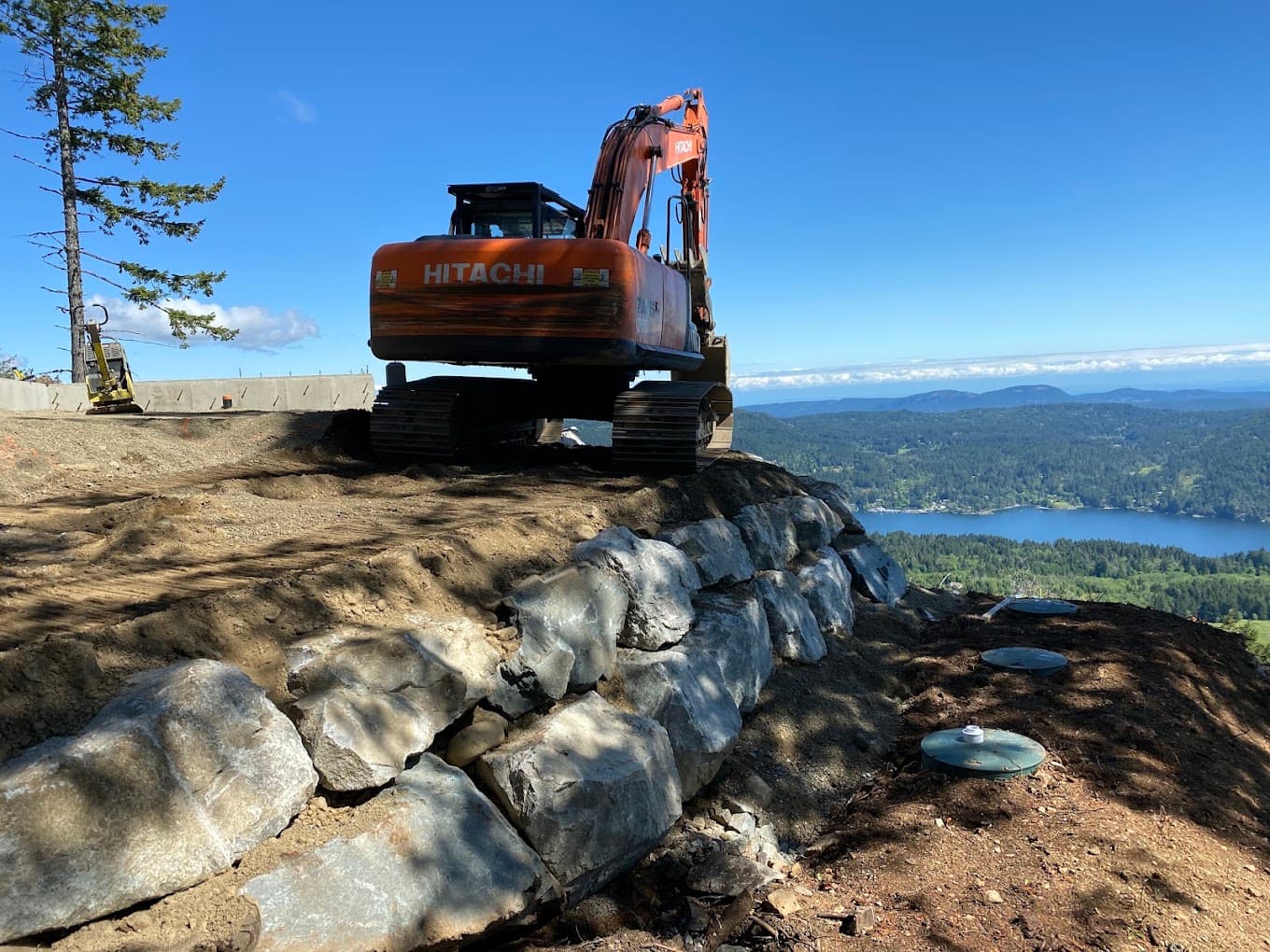 A finished septic field with green riser lids set into fresh soil, above a lake on Salt Spring Island