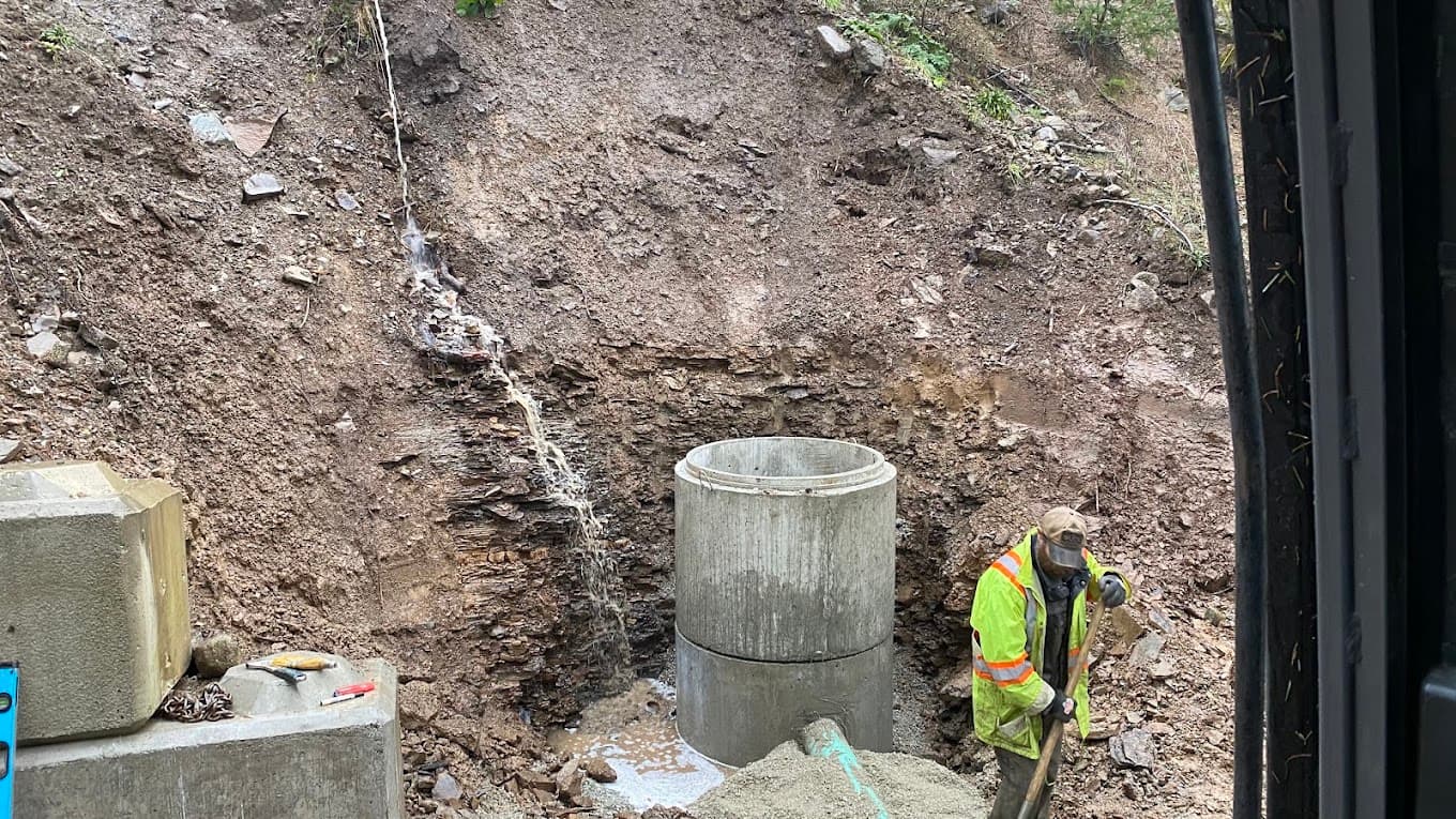 A worker setting a concrete chamber against a wet cut bank with water running through it