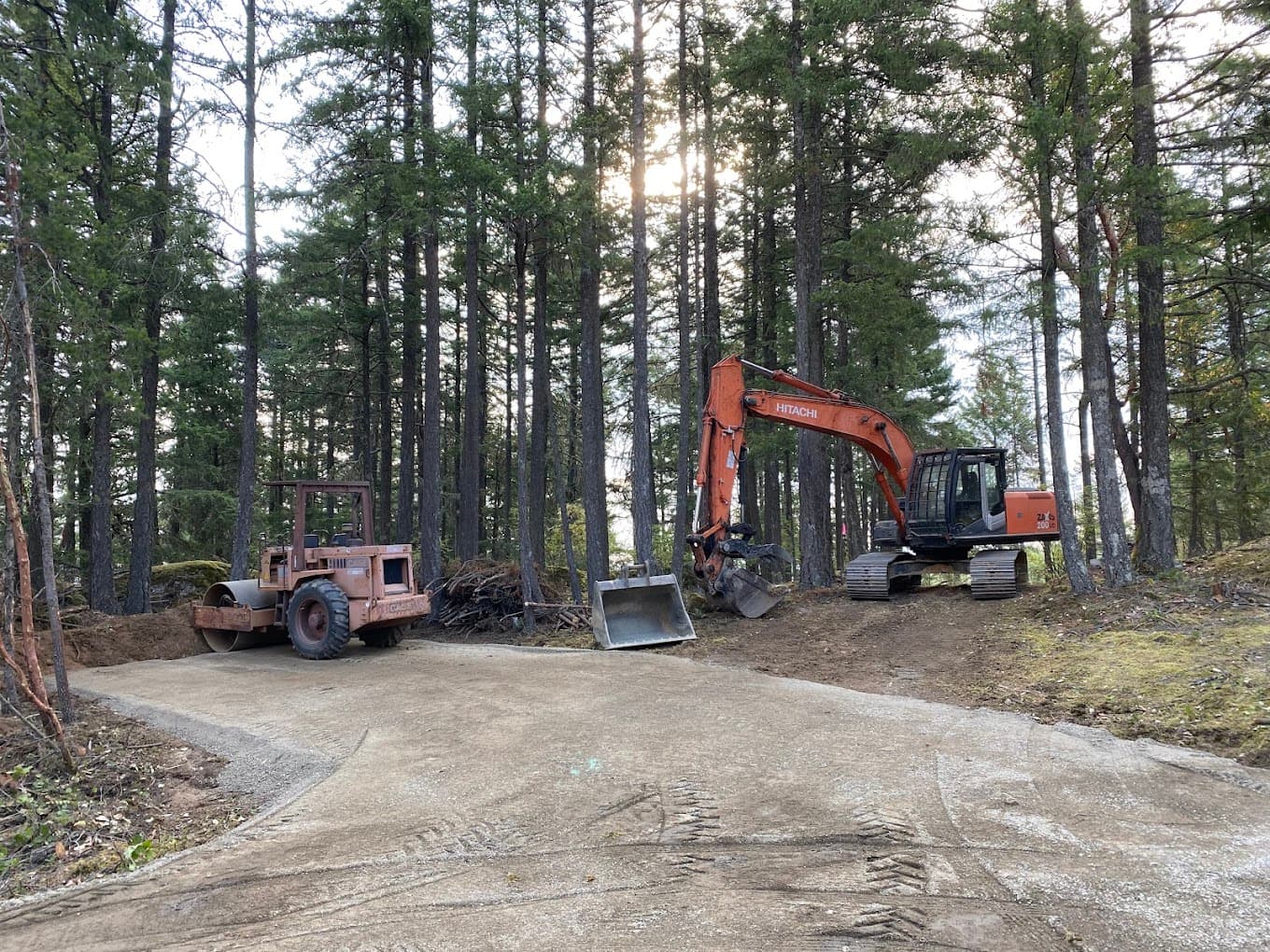A compactor and an excavator on a newly finished gravel driveway through the forest