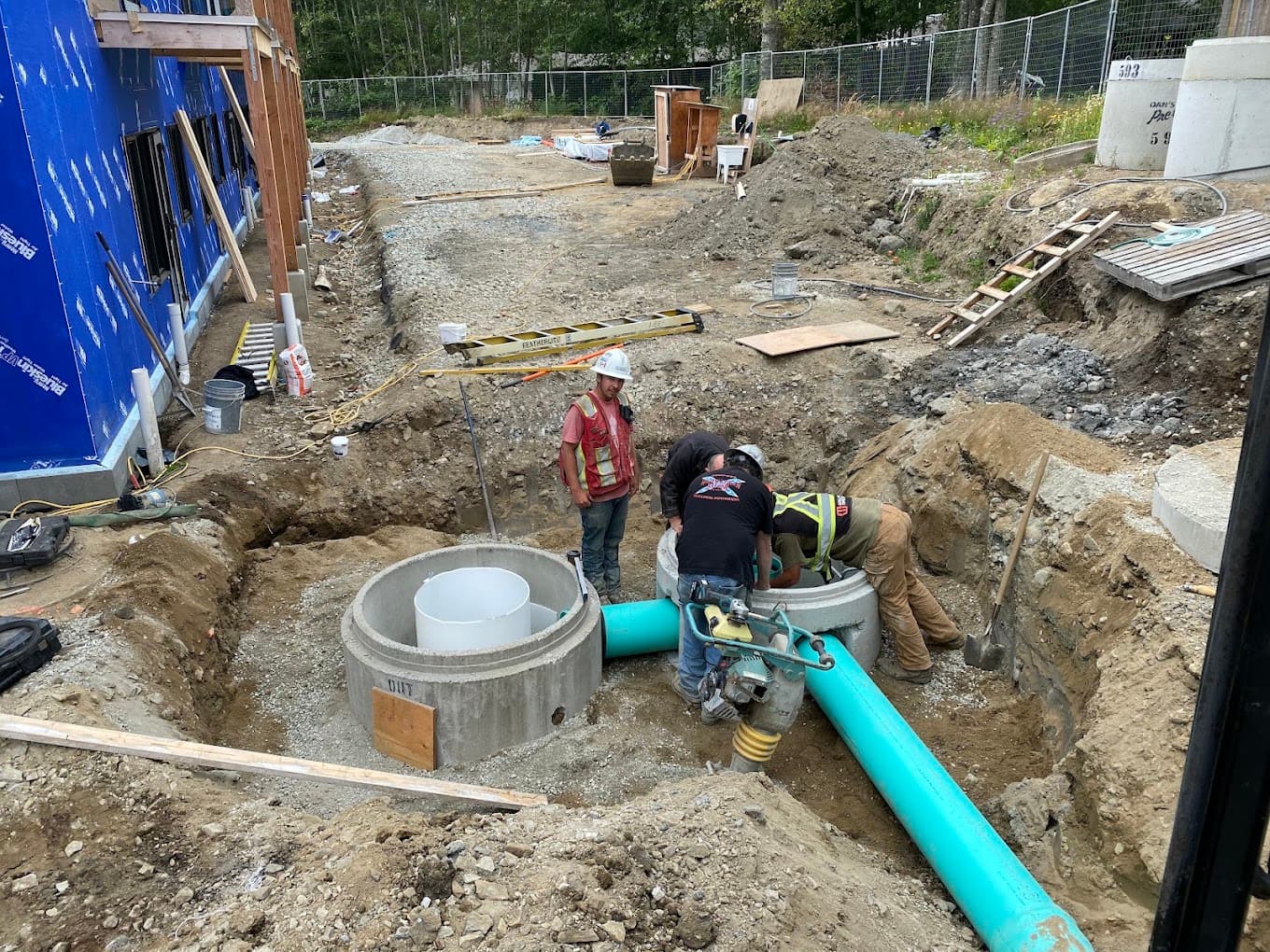 A crew setting concrete manhole sections and a large sewer main in an open trench